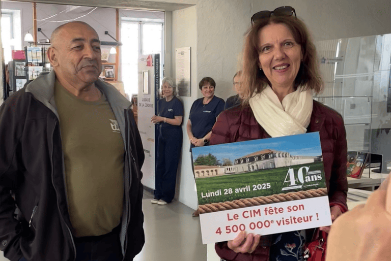 Un couple se tient à l'accueil de la Corderie Royale et tient une pancarte qui les félicite d'être 4 500 000e visiteur de ce lieu