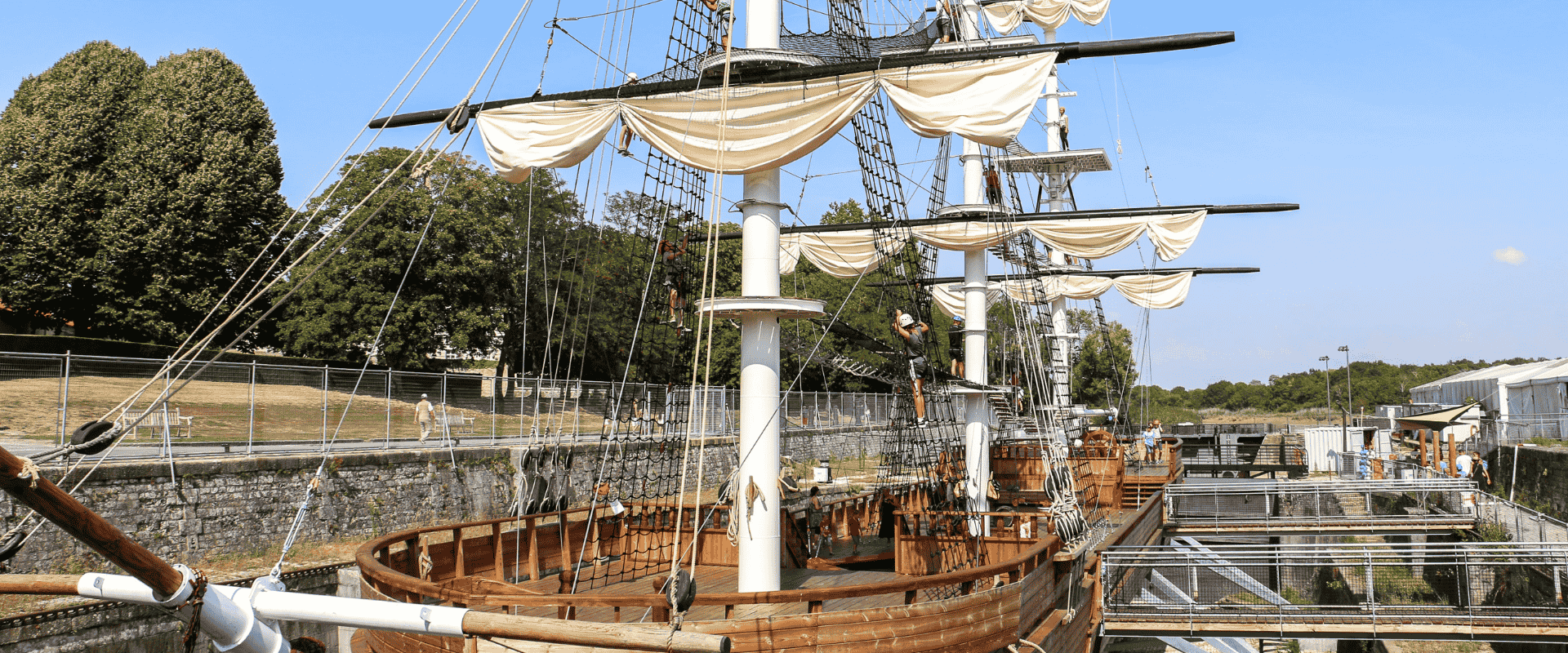 Le bateau Accro-Mâts se tient dans la forme de radoub et on aperçoit le parcours d'accrobranche.