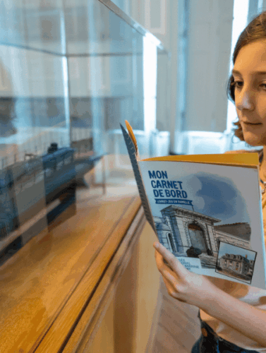 Une petite fille observe une maquette tout en lisant son livre d'activité