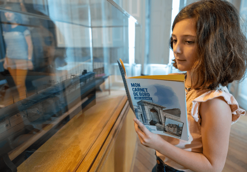 Une petite fille observe une maquette tout en lisant son livre d'activité