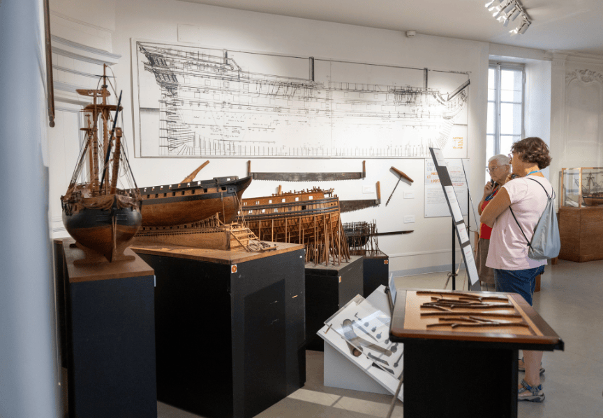 Deux personnes se tiennent face à des modèles réduits de bateaux en bois.