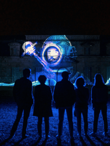 Cinq personnes se tiennent face à la Corderie Royale et admirent une illumination avec un homme en scaphandre