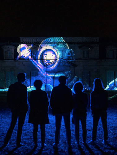 Cinq personnes sont face à la Corderie Royale et admirent la projection nocturne.